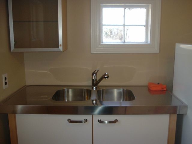 Kitchen or utility area with stainless steel double sink, white cabinetry, faucet, and a small window; neutral tones, practical setting